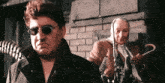 a man wearing sunglasses and a scarf is standing next to a woman holding an umbrella