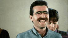 a man with a mustache is laughing with a woman behind him