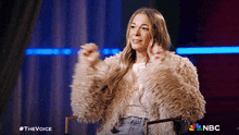 a woman wearing a fur coat is sitting in a chair with the nbc logo in the corner