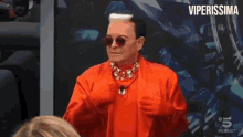 a man in a red suit and sunglasses is standing in front of a wall with the words viperissima on it