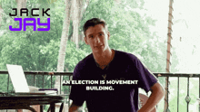 a man in a purple shirt is sitting at a table with a laptop and the words an election is movement building above him