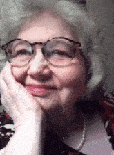 a woman wearing glasses and a pearl necklace smiles