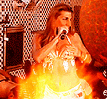 a woman is singing into a microphone in a room with flames behind her