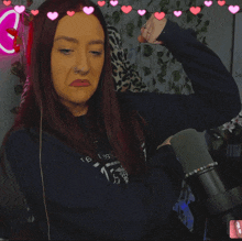 a woman flexes her muscles in front of a microphone with pink hearts around her