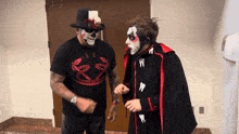 a man in a black shirt with a snake on it is standing next to a man in a black cape with teeth on it