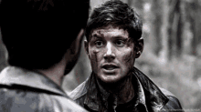 a man with blood on his face is standing next to another man in a forest .