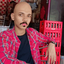a man in a pink plaid shirt is sitting in front of a coca cola crate