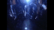 a group of people are dancing in a dark room with a blue light behind them .