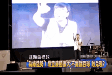 a man stands in front of a large screen that has chinese writing on it