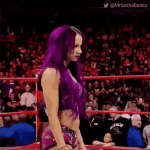 a woman with purple hair is standing in a wrestling ring with a crowd watching .