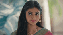 a woman wearing a necklace and earrings looks at the camera with a serious look on her face