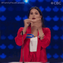 a woman in a red jacket is standing in front of a microphone and making a funny face .