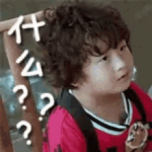 a little boy with a backpack is making a funny face with his hand in his hair .