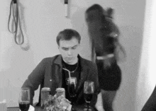 a man sits at a table with a straw in his mouth while a woman stands behind him