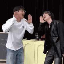 two men are standing next to each other in front of a chalkboard .