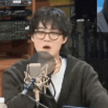 a man wearing glasses is sitting in front of a microphone with his mouth open .