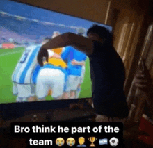 a man is standing in front of a television watching a soccer game with the caption " bro think he part of the team "
