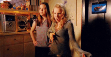 two women standing next to each other in a kitchen with a picture of a horse on the wall behind them .