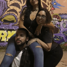 a man is carrying a woman on his shoulders in front of a graffiti wall that has the letter b on it