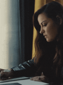 a woman in a leather jacket sits at a desk with a notebook
