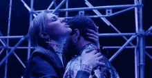 a woman is kissing a man on the neck in front of a scaffolding .