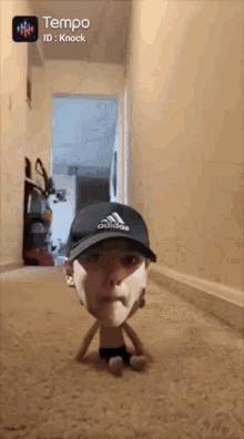 a person wearing an adidas hat is sitting on the floor in a hallway