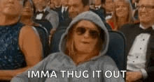 a woman in a hoodie and sunglasses is sitting in a crowd of people in a theater .