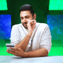 a man sitting at a table with his hands on his face looking at a phone