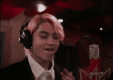 a man with pink hair is singing into a microphone in a recording studio .