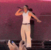 a man in a white tank top singing into a microphone on stage
