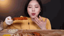 a woman in a yellow shirt is eating a piece of fried food on a stick .