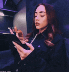 a woman in a black jacket is holding a cell phone