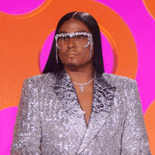 a man wearing a sequined suit and sunglasses has a cross necklace