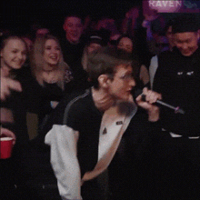 a man is singing into a microphone in front of a crowd at raven bar