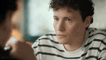 a man with curly hair wearing a striped shirt looks at another man