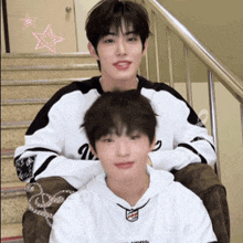 two boys are sitting on a set of stairs with one wearing a sweatshirt that says ' a ' on the front