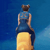 a woman in a blue and gold outfit is sitting on a yellow object with a blue background