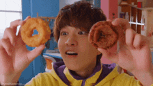 a man in a yellow hoodie holds two donuts in his hands