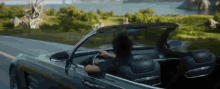 a man is driving a convertible car on a road with the top down .