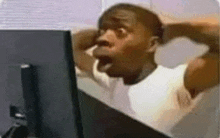 a man is sitting in front of a computer with his mouth open and his hands behind his head .
