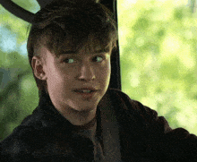 a young boy in a plaid jacket looks to the side