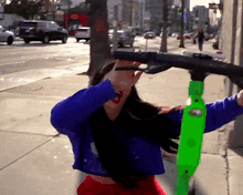 a woman in a blue shirt is holding a green scooter on a sidewalk