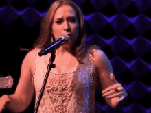 a woman is singing into a microphone while holding a guitar .