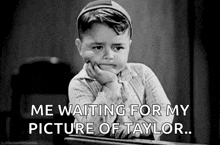 a little boy is sitting at a desk with his hand on his chin and waiting for his picture of taylor .