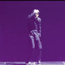 a man in a black suit is dancing in front of a purple background