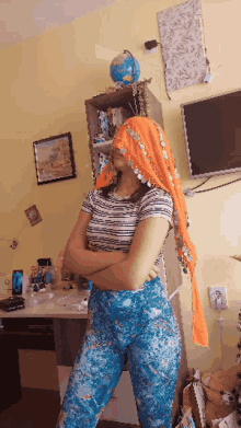a woman wearing an orange head scarf stands with her arms crossed in front of a globe