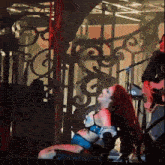 a woman with red hair is sitting on a stage with a man playing a guitar in the background