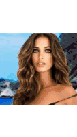 a woman with long brown hair and blue eyes is standing in front of a body of water
