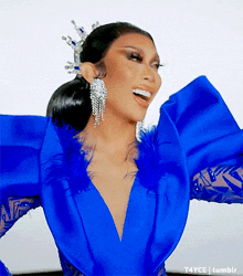 a woman in a blue dress with feathers on the sleeves is smiling .