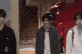 a group of young men are standing next to each other in front of a red car .